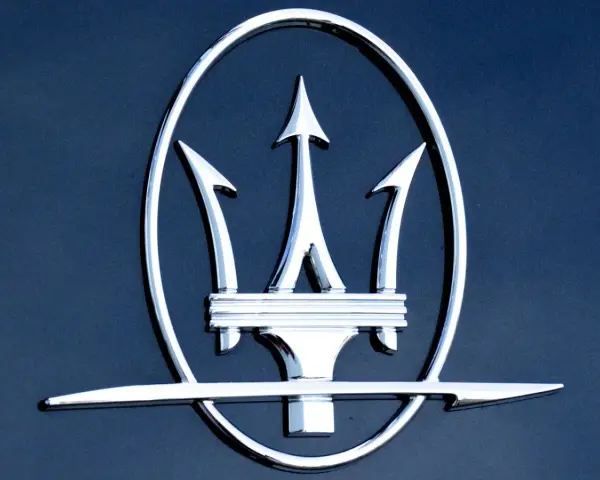 Błyszczący, chromowany trójząb Neptuna, czyli jak wygląda znaczek Maserati, na ciemnoniebieskim tle.