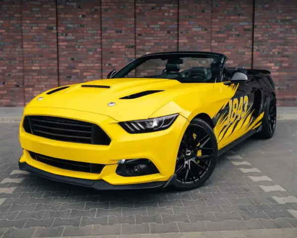 Żółty kabriolet Mustang GT 5.0 z czarnymi felgami i grafiką na boku.