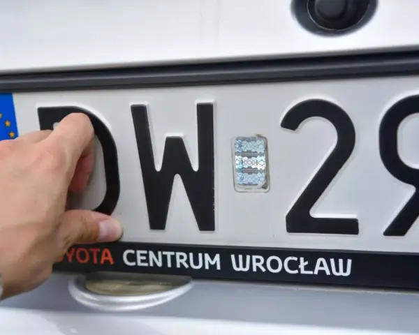 Dłoń dotyka tablicy rejestracyjnej z literami DW i numerem 29. To tablice rejestracyjne województwa dolnośląskiego.