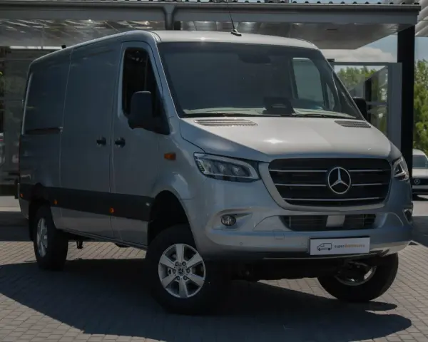 Srebrny bus Mercedes-Benz Sprinter, idealny jako jaki bus na budowę, stoi na parkingu przed nowoczesnym budynkiem.