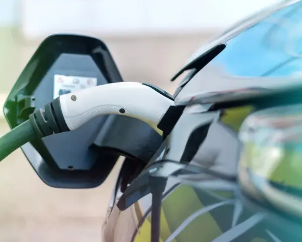 Ładowanie samochodu elektrycznego. Wtyczka podłączona do portu ładowania, zielony kabel biegnie do stacji.