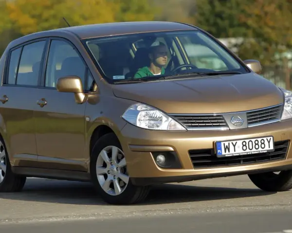 Złoty Nissan Tiida z mężczyzną za kierownicą jedzie po drodze.