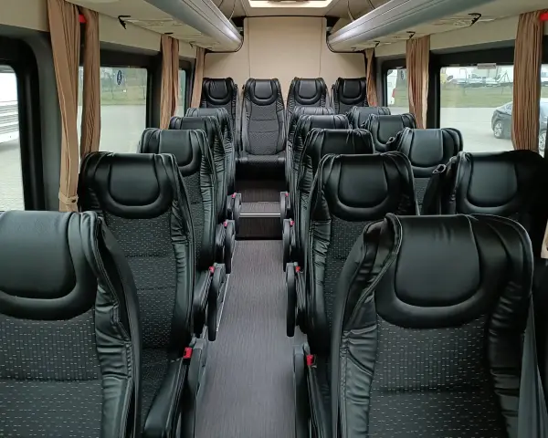 Wnętrze busa z rzędami czarnych, wygodnych siedzeń. Widać, ile miejsc ma bus osobowy, gotowy na podróż.