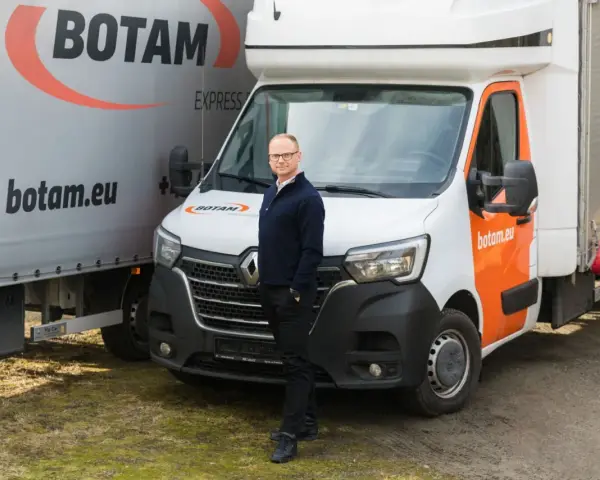 Mężczyzna stoi przed białym busem do transportu międzynarodowego marki BOTAM.