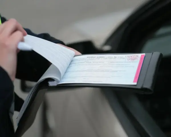 Policjant wypisuje mandat za kolizję. Dokument zawiera numer seryjny i pieczęć.