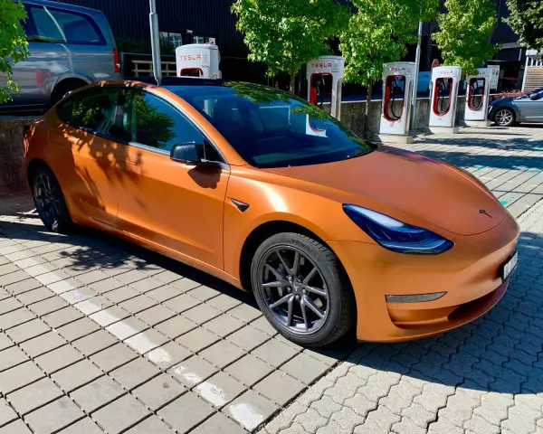 Pomarańczowa Tesla Model 3 na ładowarce. Zastanawiasz się, ile przejedzie Tesla na jednym ładowaniu?