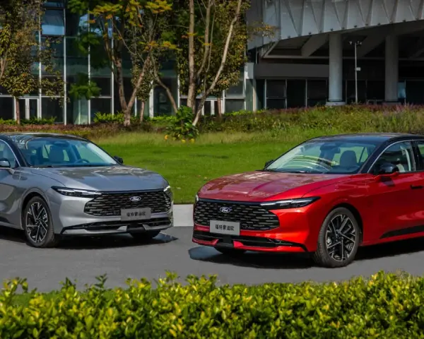 Dwa nowe Fordy Mondeo mk6, jeden czerwony, drugi szary, stoją obok siebie na tle nowoczesnego budynku i zieleni.