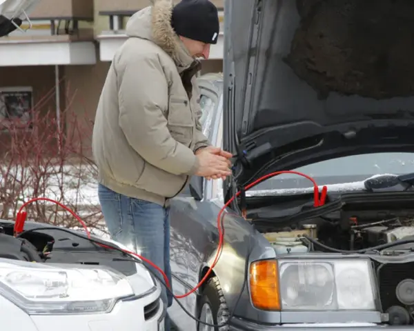 Mężczyzna podłącza kable rozruchowe do samochodu, by odpalić toyotę hybrydę na kable.