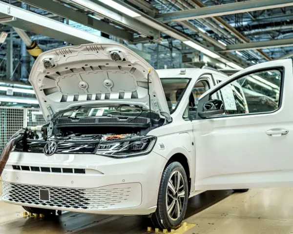 Biały samochód elektryczny na linii produkcyjnej. Widać otwartą maskę i drzwi, a także elementy silnika. Powstają tu polskie samochody.