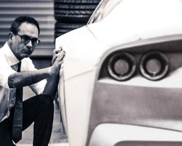 Mężczyzna w okularach i białej koszuli dopracowuje kształt prototypu, który przypomina, jak wygląda Ferrari.