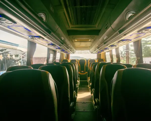 Wnętrze autobusu z rzędami zielonych siedzeń. Trudno ocenić, ile bus ma miejsc, ale wygląda na to, że jest ich sporo.