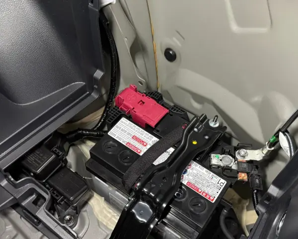 Akumulator 12V w Toyocie Prius znajduje się w bagażniku, pod plastikową osłoną. Widoczne są dwa akumulatory, jeden z czerwonym zabezpieczeniem.