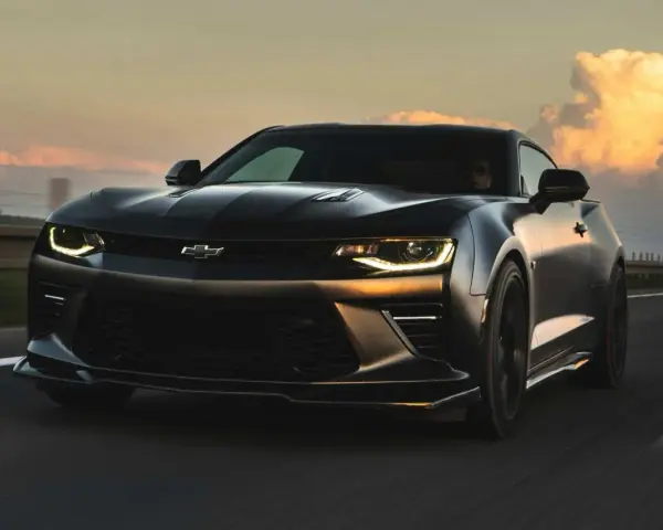 Czarny Chevrolet Camaro pędzi po autostradzie o zachodzie słońca.