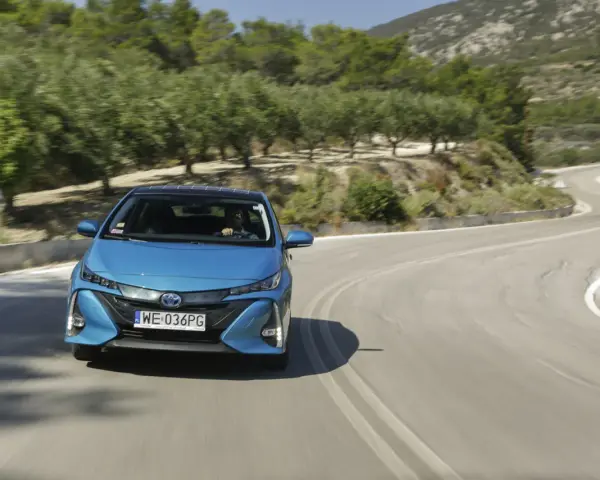 Niebieska Toyota Prius pokonuje zakręt na malowniczej drodze. Zastanawiasz się, ile pali Toyota Prius? Ten model jest znany z oszczędności.