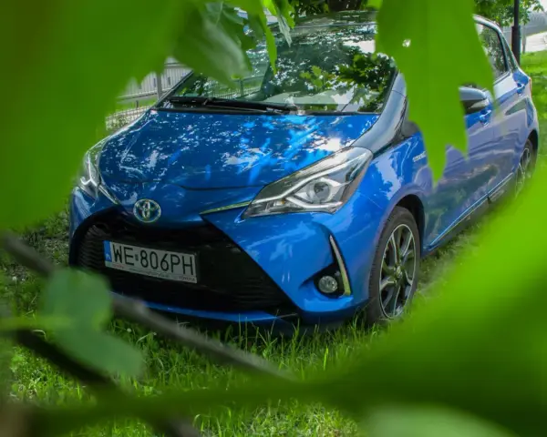 Niebieski Toyota Yaris Hybrid. Czy warto? Zobacz auto z bliska, ukryte wśród zieleni.