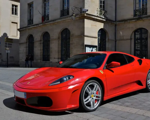 Czerwone Ferrari F430 na brukowanej ulicy przed kamienicą. Zastanawiasz się, ile kosztuje najtańsze Ferrari?