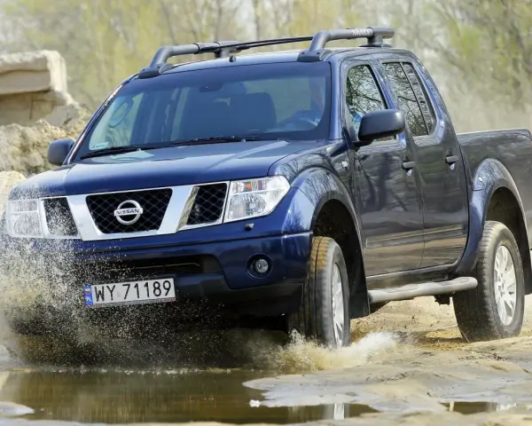 Niebieski Nissan Navara pokonuje wodną przeszkodę, wzbijając fontanny błota.