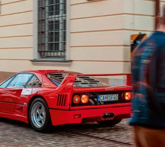 Czerwone Ferrari F40 z tablicą CA RSF40 mija pieszego na brukowanej ulicy.