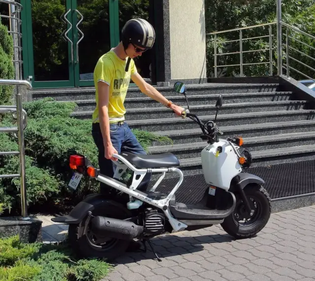 Chłopak w kasku i żółtej koszulce przy białym skuterze. Zastanawiasz się, ile kosztuje karta motorowerowa?