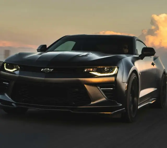 Czarny Chevrolet Camaro pędzi po autostradzie o zachodzie słońca.