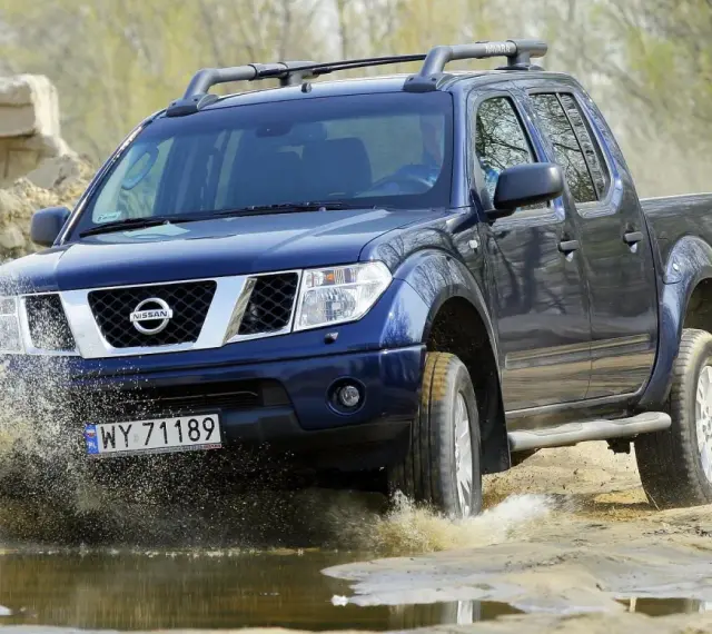 Niebieski Nissan Navara pokonuje wodną przeszkodę, wzbijając fontanny błota.