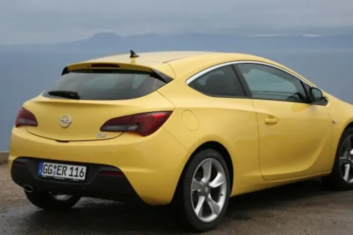Żółta Astra GTC z tablicą rejestracyjną GG ER 116 stoi na tle morza i gór.