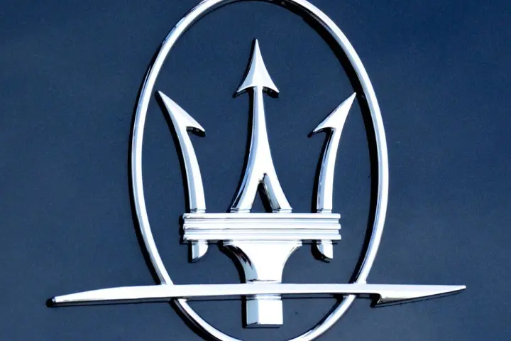 Błyszczący, chromowany trójząb Neptuna, czyli jak wygląda znaczek Maserati, na ciemnoniebieskim tle.