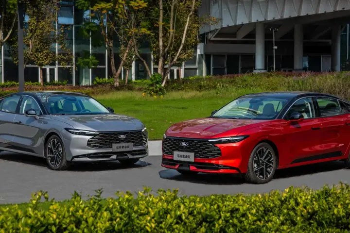Dwa nowe Fordy Mondeo mk6, jeden czerwony, drugi szary, stoją obok siebie na tle nowoczesnego budynku i zieleni.