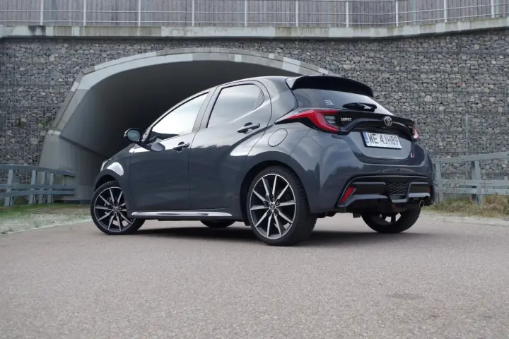 Szary Toyota Yaris GR Sport z czarnym spojlerem i dyfuzorem, zaparkowany przed tunelem.