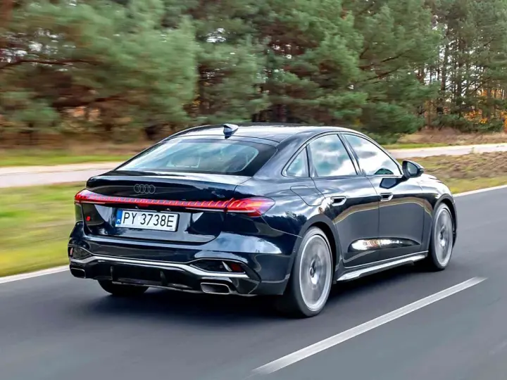 Ciemny Audi A4 B10 pędzi po drodze, otoczony jesiennym lasem.