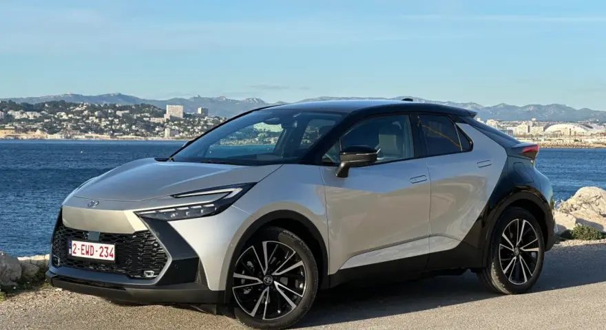 Srebrno-czarna Toyota C-HR na tle morza i miasta. Zastanawiasz się, ile przejedzie hybryda Toyoty na jednym ładowaniu?