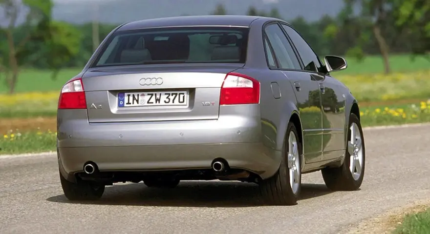 Srebrne Audi B6 sedan z tablicą rejestracyjną IN ZW 370 jedzie po asfaltowej drodze wśród zieleni i żółtych kwiatów.