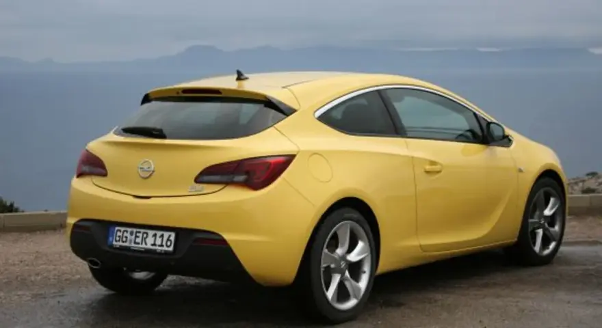 Żółta Astra GTC z tablicą rejestracyjną GG ER 116 stoi na tle morza i gór.