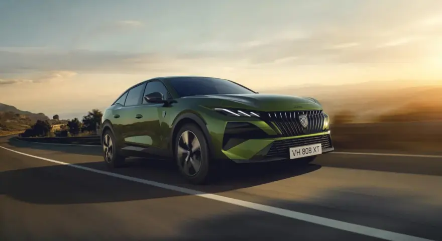 Zielony Peugeot 408 GT sunie po krętej drodze, otoczony malowniczym krajobrazem o zachodzie słońca.