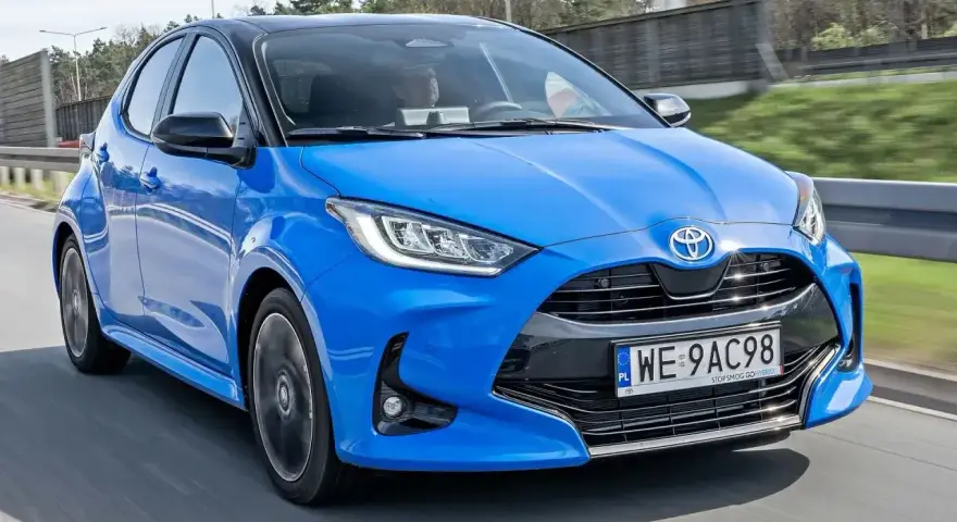Błękitna, nowa Toyota Yaris z czarnym dachem pędzi po drodze.
