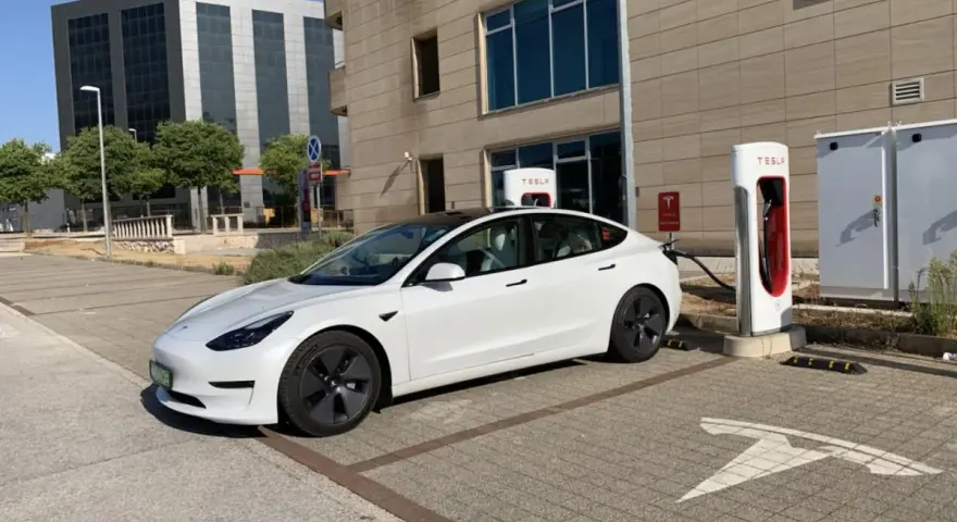 Biały Tesla Model 3, zasilany energią, czeka na ładowanie. Zastanawiasz się, ile koni ma ten model?