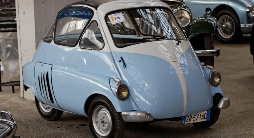 Urocze, błękitno-białe BMW Isetta z lat 50. z charakterystycznymi drzwiami z przodu, gotowe na przejażdżkę po mieście.