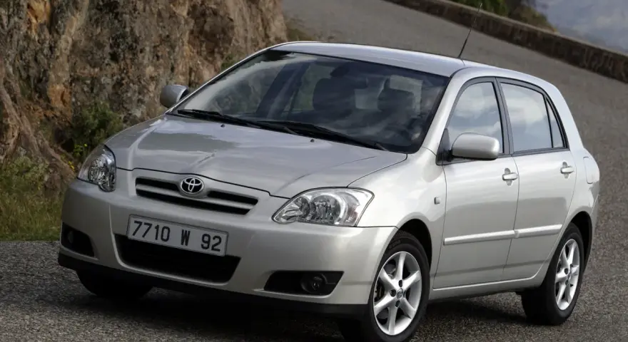 Srebrna Toyota Corolla E12 na krętej drodze, z kamienistym zboczem w tle.