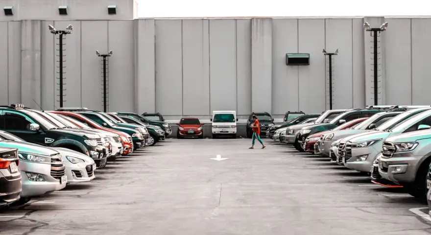 Rząd samochodów na parkingu, jedna osoba idzie pośrodku.