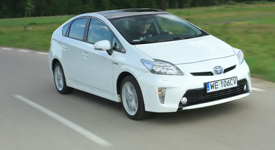 Biała Toyota Prius w ruchu. Czy warto kupić ten hybrydowy samochód?