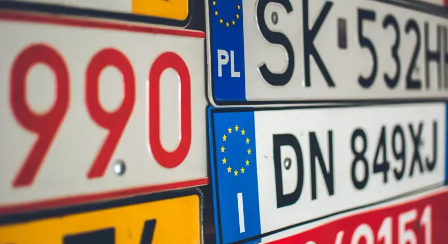 Zbliżenie na stos tablic rejestracyjnych z różnymi kody samochodowe. Widoczne numery to m.in. 990, SK 532HH, DN 849XJ.