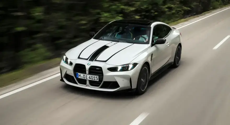 Białe BMW M4 z czarnymi pasami na masce pędzi po krętej drodze. Zastanawiasz się, ile kosztuje BMW M4?