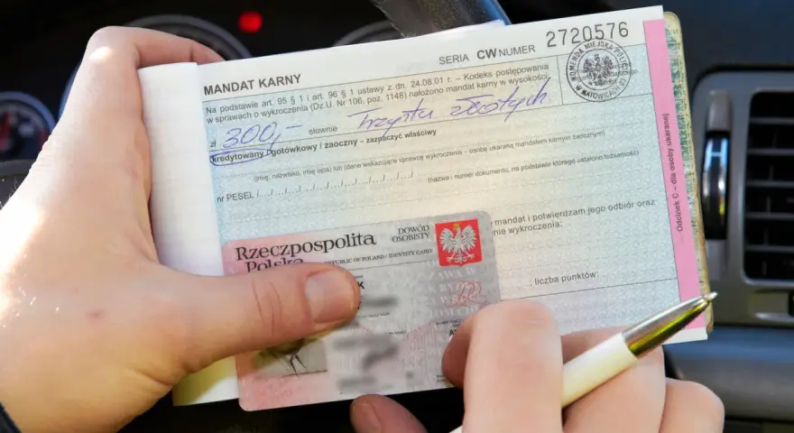 Ręka trzyma mandat karny na 300 zł i dowód osobisty. Ktoś wypełnia dokument, być może to mandat za parkowanie.