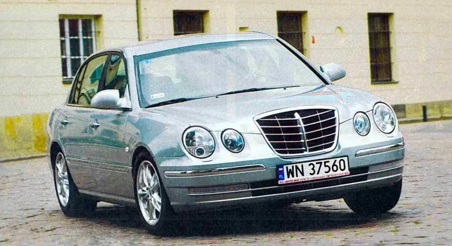 Srebrny Kia Opirus z polskimi tablicami rejestracyjnymi WN 37560 na brukowanej ulicy.