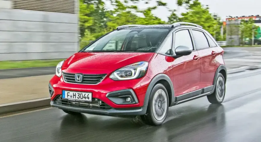 Czerwony Honda Jazz 4 w wersji Crosstar z czarnym dachem i relingami, porusza się po mokrej drodze.