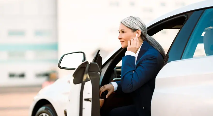 Elegancka kobieta w garniturze wsiada do białego auta. To jej auto na abonament, idealne do biznesowych podróży.