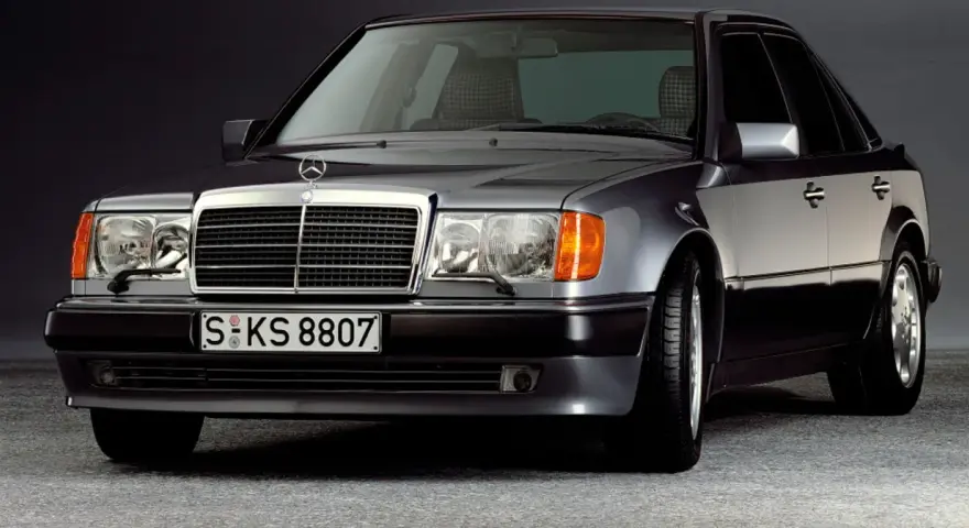 Klasyczny youngtimer, szary Mercedes-Benz W124 z charakterystyczną kratką i reflektorami.