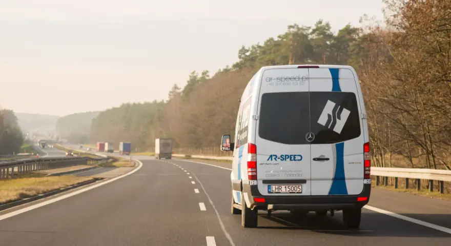 Biały bus AR-SPEED jedzie autostradą. Zastanawiasz się, ile kosztuje bus do Niemiec? Sprawdź na ar-speed.pl.