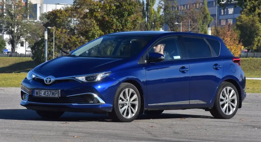 Niebieska Toyota Auris Hybrid, z kierowcą za kierownicą, na parkingu. Zastanawiasz się, ile pali Toyota Auris Hybrid?