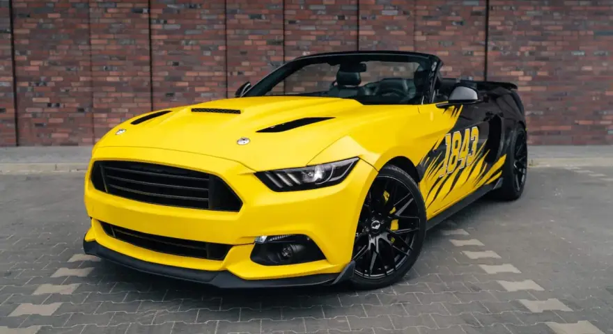 Żółty kabriolet Mustang GT 5.0 z czarnymi felgami i grafiką na boku.